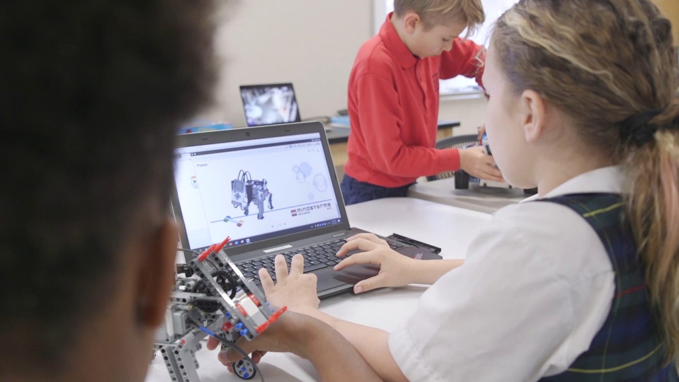 Over-the-shoulder view of students coding at a laptop with a half-built robot in front.