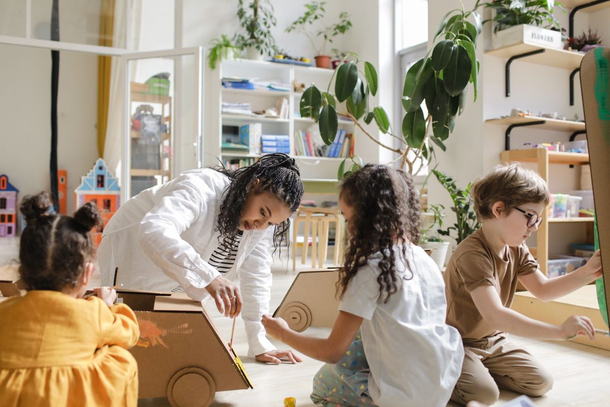 Young kids and a teacher build a vehicle out of cardboard