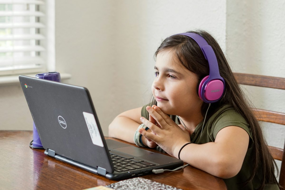 A girl in headphones concentrates on a game on her laptop