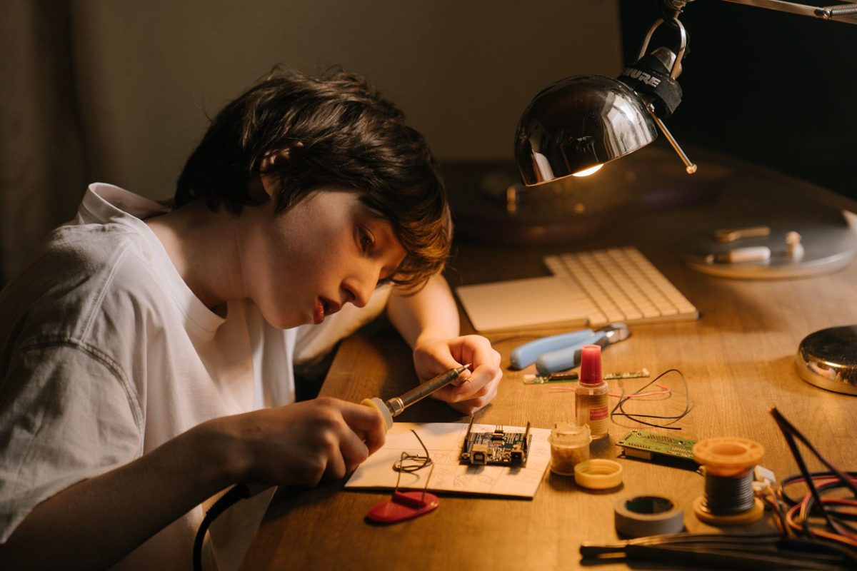 A student solders a circuit board under a warm lamp