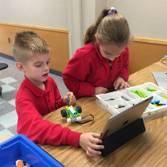 Two young students test a small LEGO vehicle they programmed on a tablet