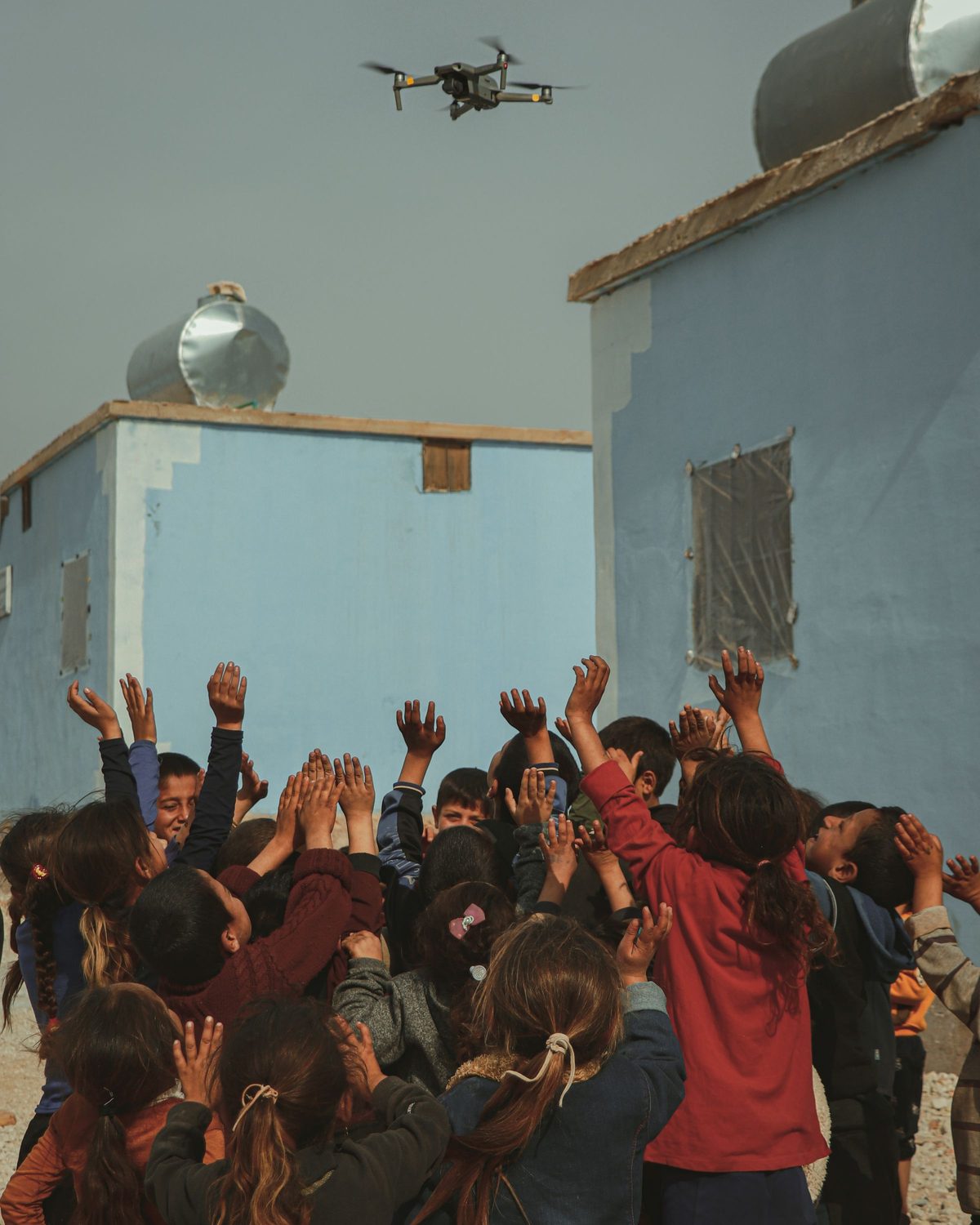 Kids reach up toward a small flying drone