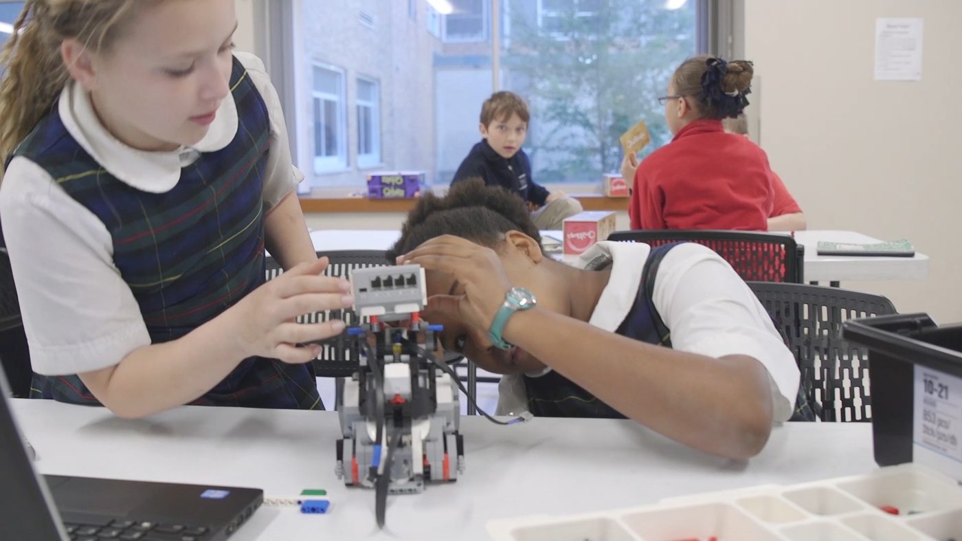 Two girls adjust the sensor on their LEGO robot.
